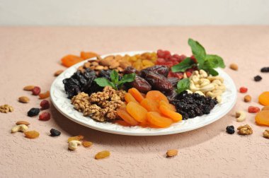 Büyük beyaz bir tabak üzerinde fındık ve kurutulmuş meyve. Kuru üzüm, kuru kayısı, kuru erik, hurma, kiraz, kaju fıstığı, badem, ceviz bir tabak üzerinde. Açık arka plan. Close. 