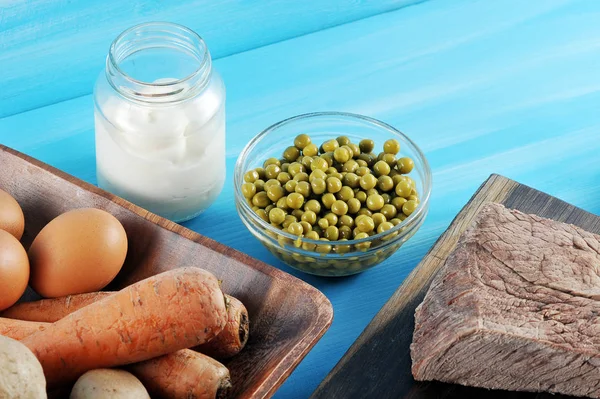 Salata olivier hazırlanması için ayarlayın. Çerçeveiçinde haşlanmış yumurta, patates, havuç, salatalık turşusu ile bir tabak vardır. Mayonez konservesinin yanında, bir tabak bezelye ve haşlanmış sığır eti. Mavi arka plan