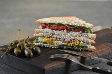 Yarım ton balıklı sandviç. Sandviçin yanında kapari var. Çatal. Karanlık arka plan. Close. Makro çekimi.