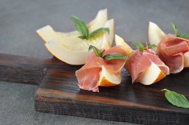 Kavun dilimleri ile Prosciutto. Fesleğen yaprakları ile dekore edilmiş geleneksel İtalyan meze. Close. Makro çekimi. Koyu arka plan.