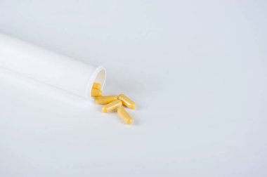 Sarı kapsüller beyaz plastik şişeden dökülür. Ağızdan kullanım için tabletler. Sağlık konsepti. Metin yerleştirme alanı. Close. Beyaz arka plan.