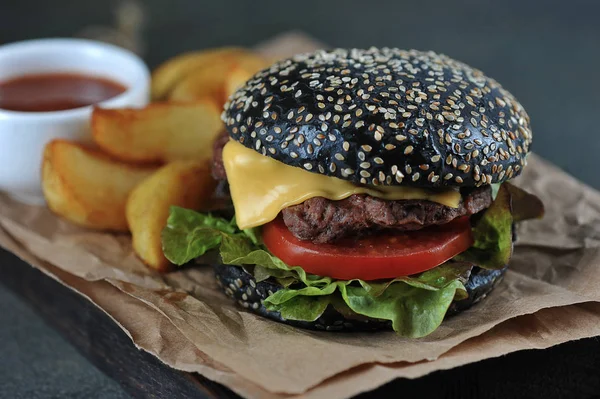 Black burger with cheese, lettuce, beef patty, slice of tomato. Idaho potatoes and  Sauce complement the hamburger. Macro shooting. Dark background.