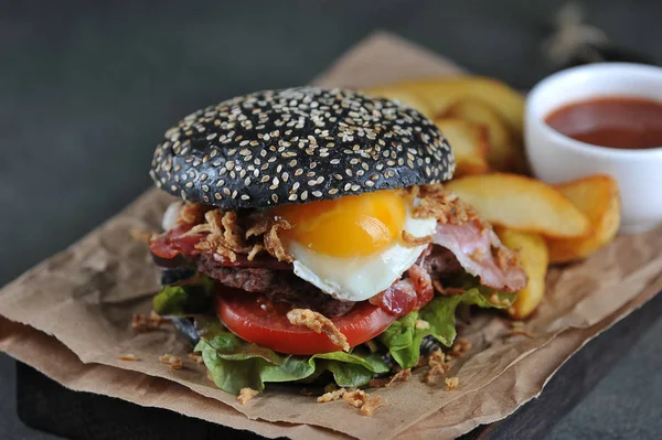 Black burger with fried egg. In the burger filling bacon and onion chips. Dark background. Close-up. Macro shooting.