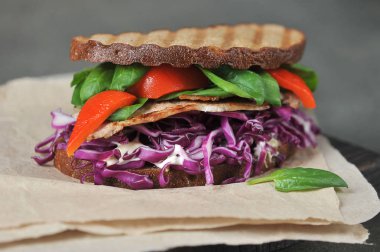 Koyu ekmekli sandviç. Sandviç dolgu et, kırmızı lahana, ıspanak ve kırmızı biber, ızgara üzerinde pişmiş oluşur. Close. Koyu arka plan.