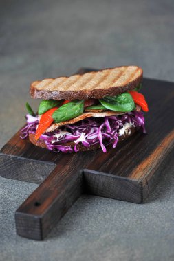 Etli sandviç, kırmızı lahana, ıspanak ve ızgara kırmızı biber. Close. Karanlık arka plan. Çerçevenin dikey yönü.
