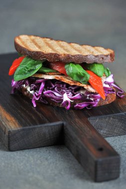 Etli sandviç, kırmızı lahana, ıspanak ve ızgara kırmızı biber. Close. Karanlık arka plan. Çerçevenin dikey yönü.