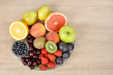 Acceptable fruits for diabetes. In a plate are orange, grapefruit, cherry, plum, pears, peaches, apple, plum, blueberries, kiwi. View from above. Light background. Free space for text. clipart