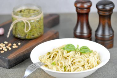 Pesto ve fesleğenli makarna. Yakınlarda bir kavanoz pesto, sarımsak, fındık ve baharatlar. Öğle yemeği masa ayarı konsepti. Karanlık arka plan. Close.