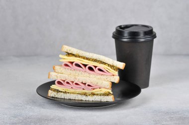 Bir tabaktabakta jambon, omlet ve peynirli sandviç. Sandviçin yanında kahveli kağıt bir fincan var. Fast food ve kahve kavramı gitmek. Açık arka plan. Close. Metin için boş alan.