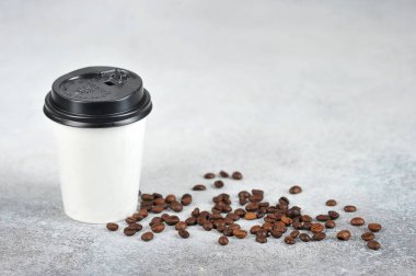 Kahveli kağıt bardak. Kağıt bardak beyaz, kapağı siyah. Yüzeyde kahve çekirdekleri var. Fast food ve kahve kavramı gitmek. Açık arka plan. Close. Metin için boş alan.