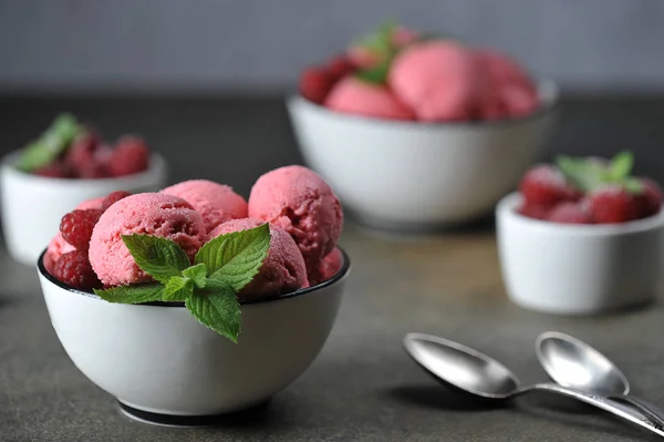 Cup with balls of berry ice cream. Ice cream decorated with fresh raspberries and mint leaves. Dark background. Free space to place text.