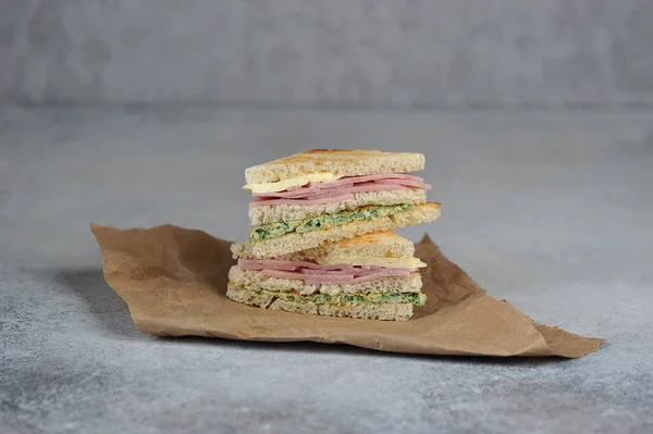 Sandwiches of white bread on Kraft paper. Sandwich stuffing consists of ham, cheese and scrambled eggs with spinach.