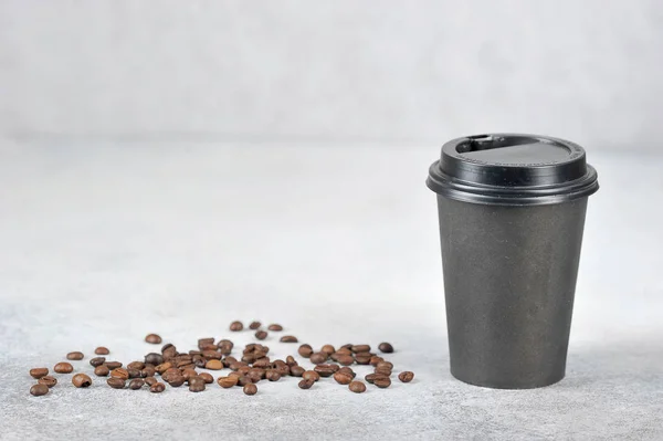 Paper cup with coffee. The paper cup is black, the lid is black plastic. Coffee beans on the surface. The concept of fast food and coffee to go. Light background. Free space for text.
