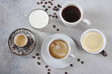 Farklı fincanlarda kahve farklı türde ayarlayın. Espresso, kapuçino, Americano, latte sunulmaktadır. Hafif bir masanın yüzeyinde kahve çekirdekleri. Yukarıdan görüntüle.