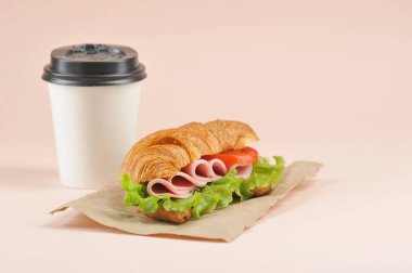 Beyaz kağıt bardakta kahve ve jambonlu sandviç. Açık ahşap arka plan. Close. Metin için boş alan.