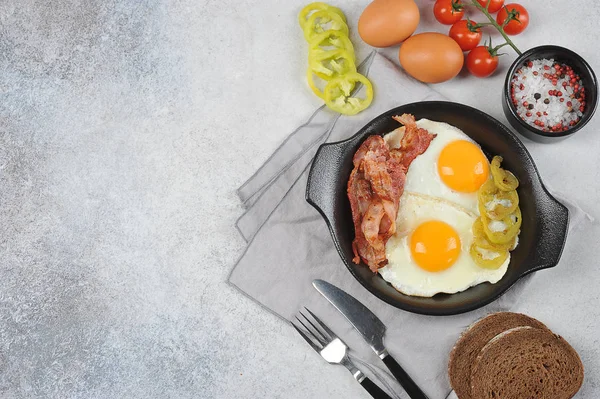 Fried eggs with bacon in a pan. Light background. View from above. Free space for text.