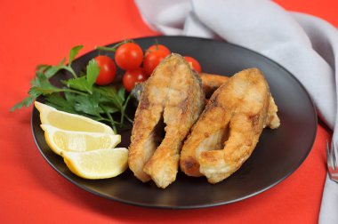 Siyah tabakta sazan bifteği. Limon dilimleri, kiraz domates ve maydanoz kızarmış balık çanak tamamlamak. Kırmızı arka plan. Close.