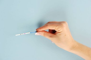 Kadın elinde gebelik için test şeridi. Test şeridinde pozitif bir sonuç. Mavi arka plan. Close.