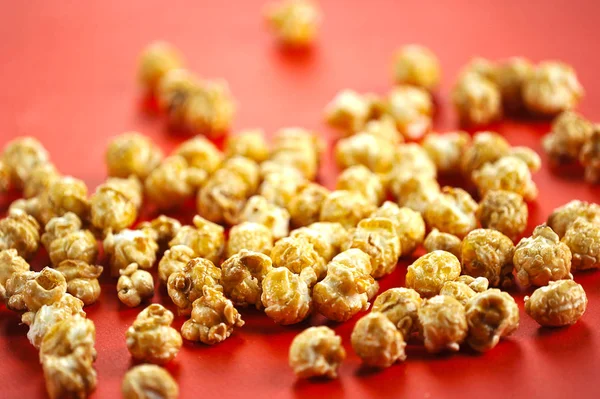 Caramel popcorn is scattered on a red surface. Popcorn takes up the entire frame space. Close-up.