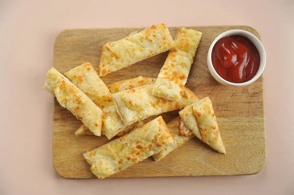 Cheese sticks on a wooden tray. Next to the cup with red sauce. Light background. View from above. Close-up.