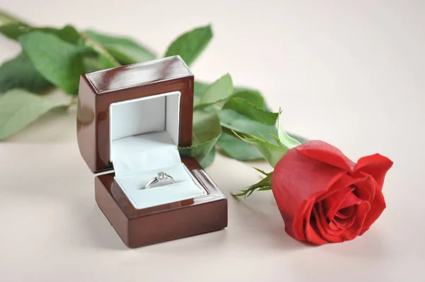 Ring with a diamond in a gift box. Next to the box is a red rose. The perfect holiday gift. Light background. Close-up. Macro shooting.