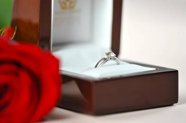 Ring with a diamond in a gift box. Next to the box is a red rose. The perfect holiday gift. Light background. Close-up.