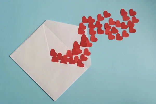 Congratulations on St. Valentine\'s Day. Many red hearts in a white postal envelope. Blue background. Close-up.  View from above. Free space under the text.