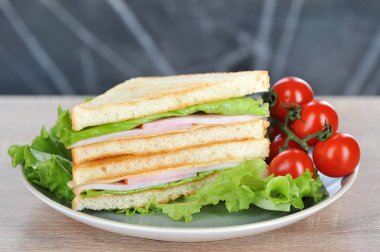 Tabakta peynir li ve jambonlu sandviç. Salata yaprakları ve bir tabakta kiraz domates dalı. Açık arka plan. Close. Makro çekimi.