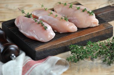 Raw chicken breast on a wooden board. The fillet is decorated with thyme sprigs. The composition is complemented with a cloth and green thyme. Light wooden background. Close-up. Macro shooting. clipart