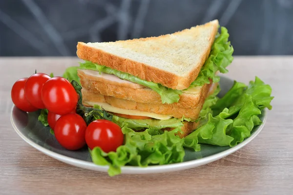 Sandwich with cheese and party. White bread is used to make a sandwich. On a plate with sandwich cherry tomato branch and lettuce leaves. Close-up.