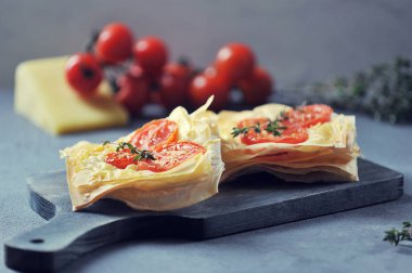 Peynir ve domates ile puf böreği mini pizza. Kompozisyon kiraz domates, peynir ve kekik ile tamamlanmaktadır. Gri arka plan. Makro çekimi. Fotoğraf vintage tarzında işlenir.