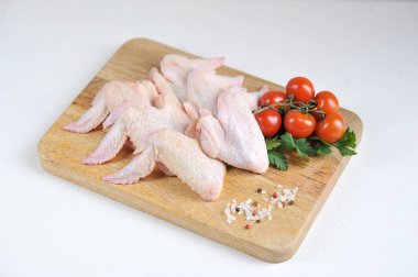 Raw chicken wings on a wooden board. The composition is complemented by cherry tomatoes, parsley and spices. White background. Close-up.  clipart