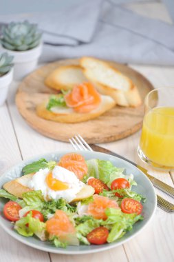 Hafif tuzlu somon ile yeşil salata. Haşlanmış yumurta ile salata tost ile tabakta. Meyve suyu ve bruscheta bir tabak ile bir bardak çerçevesinde. Açık arka plan. Close. Dikey çerçeve yönlendirmesi.