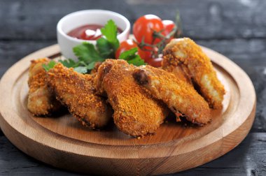 Chicken wings with crispy crust. The composition is complemented by cherry tomatoes, parsley and a cup  with ketchup sauce. Dark wooden background. Close-up.  clipart