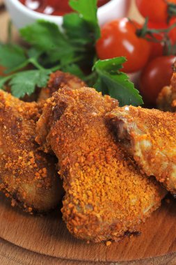 Tahta bir tahta üzerinde gevrek ekmek tavuk kanatları çerçevenin tüm alanı kaplar. Kompozisyon kiraz domates tamamlayıcı. Dikey çerçeve yönlendirmesi. Close. Makro çekimi.