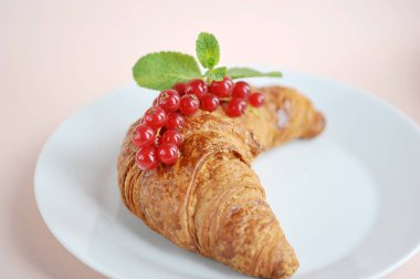 Beyaz tabakta kırmızı kuş üzümü olan kruvasan. Hafif bej arka plan. Close. Makro çekimi.