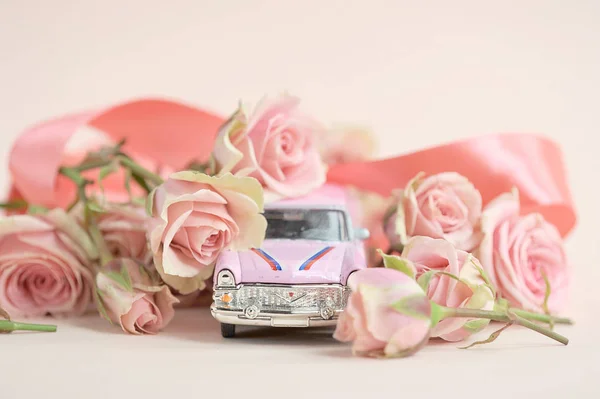 Pink toy car surrounded by a bouquet of spray roses. The concept of holiday greetings. Close-up. Light background.