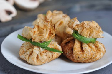 Kıymalı mantarlarla doldurulmuş bir çanta şeklinde krep. Koyu bir arka plan üzerinde krep ile beyaz tabak. Champignons arka planda dilimleri. Makro çekimi.