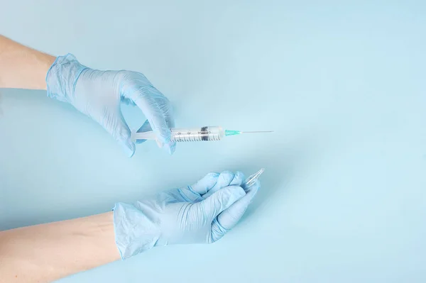 A set of drugs from the ampoule in the syringe. Ampoule in one hand. Syringe for injection in the other hand. Hands of a medical worker in latex gloves. Close-up. Light background.