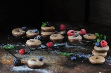 Pudra şekeri ile çörekler. Donutlar nane ve taze ahududu meyveleri, yaban mersini ve böğürtlen ile dekore edilmiştir. Koyu arka plan. 
