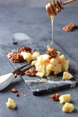 Gri bir taş tahta üzerinde parmesan peyniri ve ceviz dilimleri. Snack kaşıktan bal döktü. Gri arka plan. Close. Dikey fotoğraf yönlendirmesi.