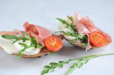 Bruschetta prosciutto ve mozzarella ile. Atıştırmalık arugula ve bir dilim domates ile dekore edilmiştir. Açık arka plan. Close.