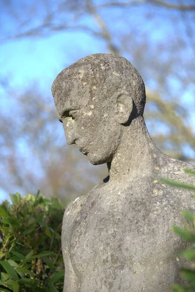 Stone figure in front of a green hedge