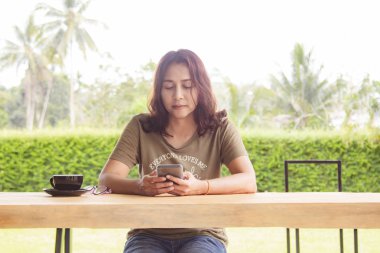 Kafede masa ve kahve fincanı üzerinde boş ekran ile siyah cep telefonu tutan kadın elleri