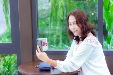 Kafede masa ve kahve fincanı üzerinde boş ekran ile siyah cep telefonu tutan kadın elleri