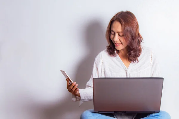 Beyaz arka plan üzerinde izole çapraz bacaklar ile katta otururken dizüstü bilgisayar üzerinde çalışan mutlu gülümseyen asyalı kadın