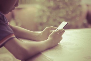 Ahşap masada akıllı telefon ile oynayan genç çocuk tek başına.