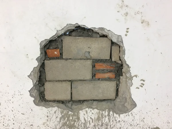 Çatlak delikli beyaz duvarda patlama. Duvarı tuğlayla onarıyorum.