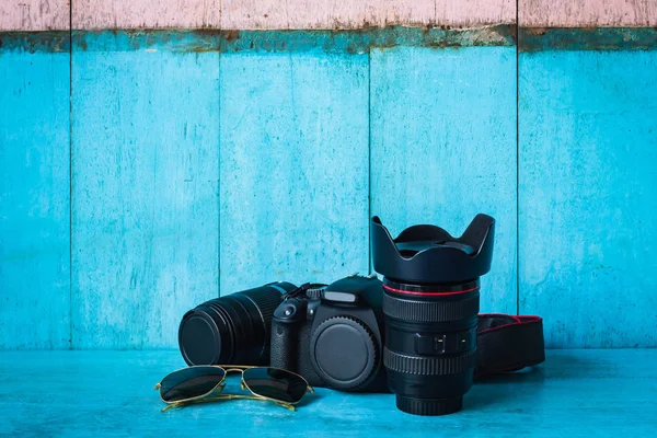Mavi ahşap masa üzerinde dijital kamera ve lens açık mavi ve pembe arka plan duvarı