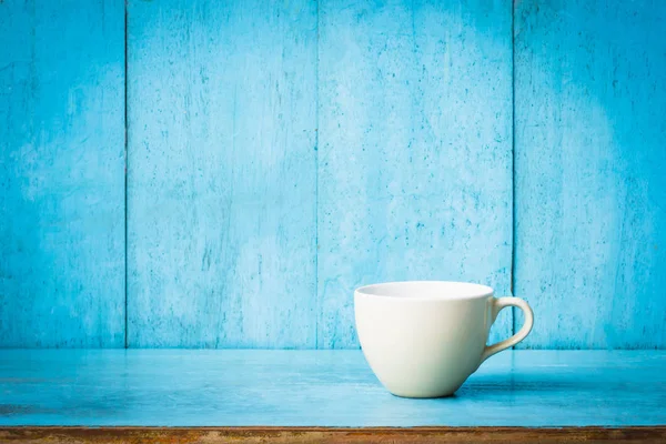 Mavi ahşap bir masada bir fincan kahve ve açık mavi arka plan duvarı.